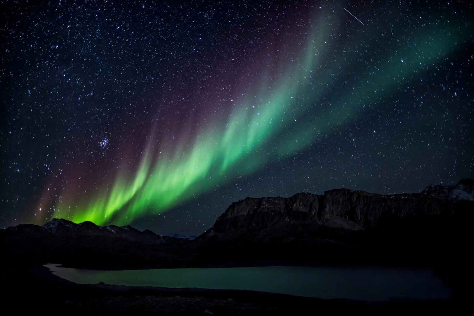 A green and purple aurora borealis over mountains.