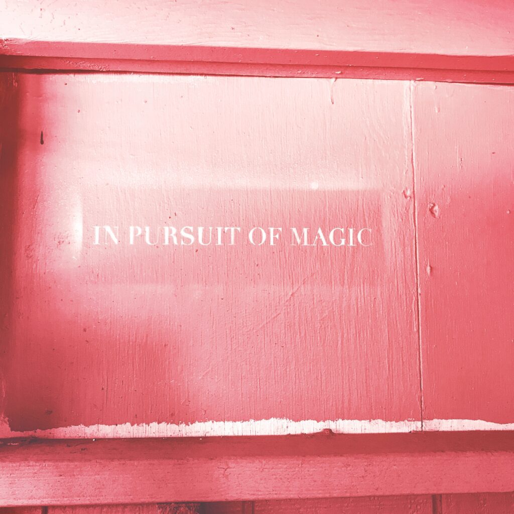 A pink wall with the words in pursuit of magic written on it.